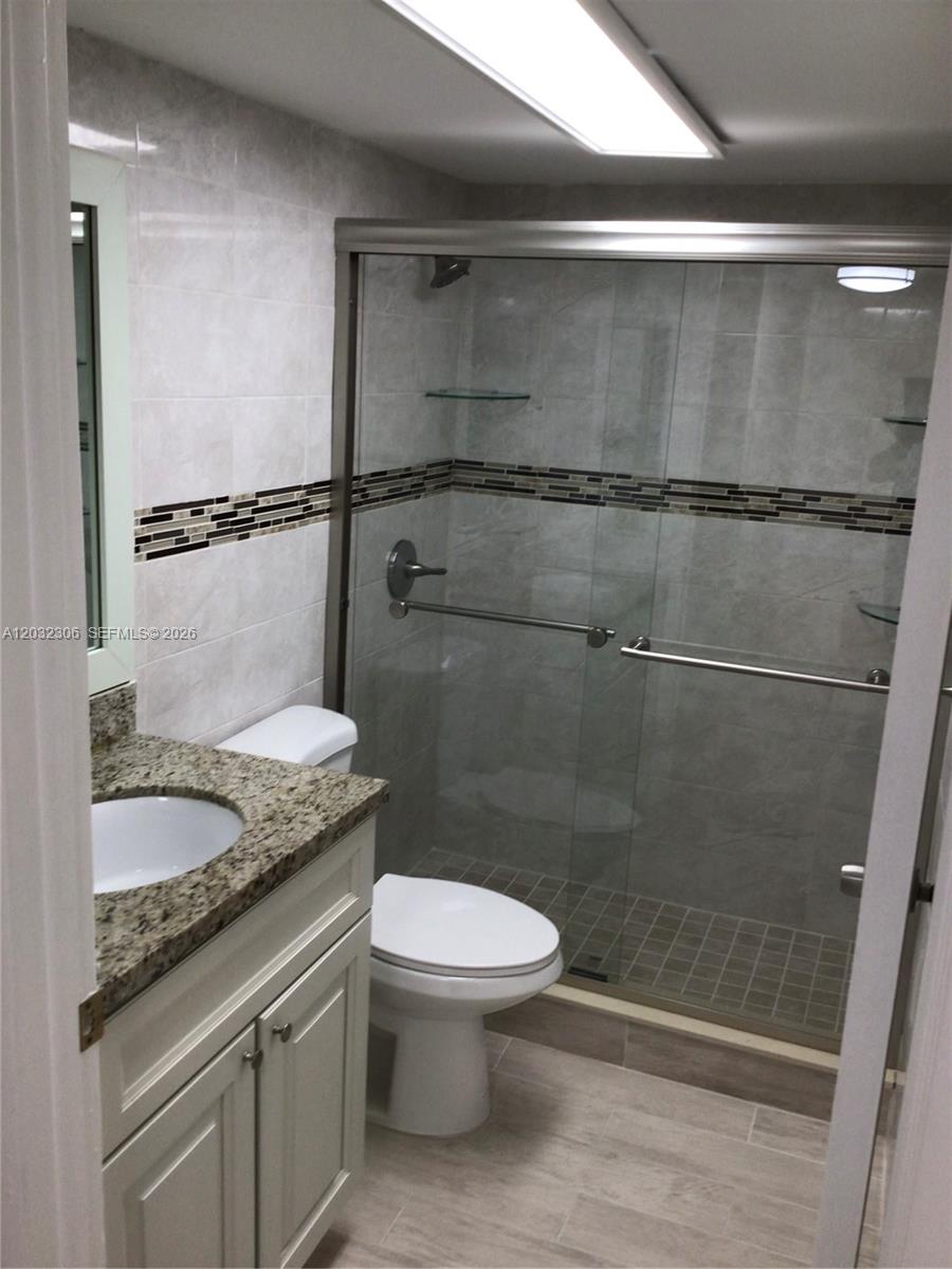 A bathroom features a granite-topped vanity, a white toilet, and a glass-enclosed walk-in shower — 10975 SW 107th St # 302, Miami FL 33176, MIAMI, FL