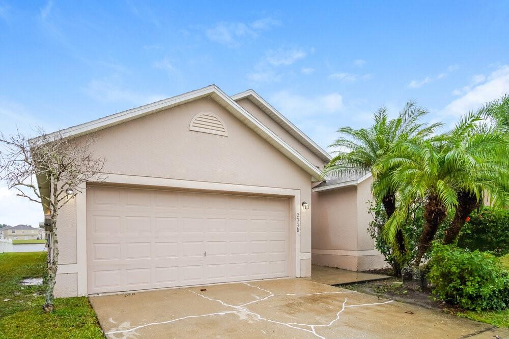 A beige single-story house with a two-car garage and a palm tree in the front — 2338 ANDREWS VALLEY DRIVE, KISSIMMEE, FL