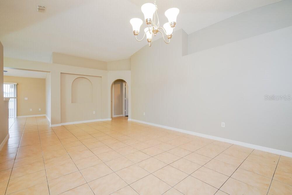 A spacious living room features light-colored tile flooring, a vaulted ceiling, and a chandelier — 2338 ANDREWS VALLEY DRIVE, KISSIMMEE, FL