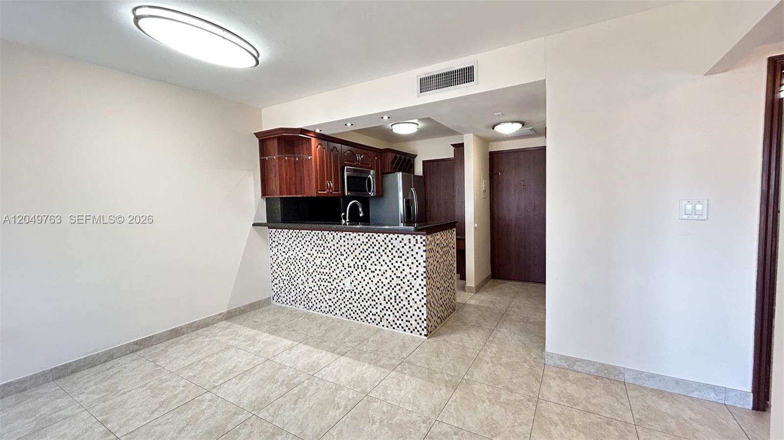 A kitchen with a tiled breakfast bar, dark wood cabinets, and light-colored floor tiles — 2899 Collins Ave # 938, Miami Beach FL 33140, MIAMI BEACH, FL