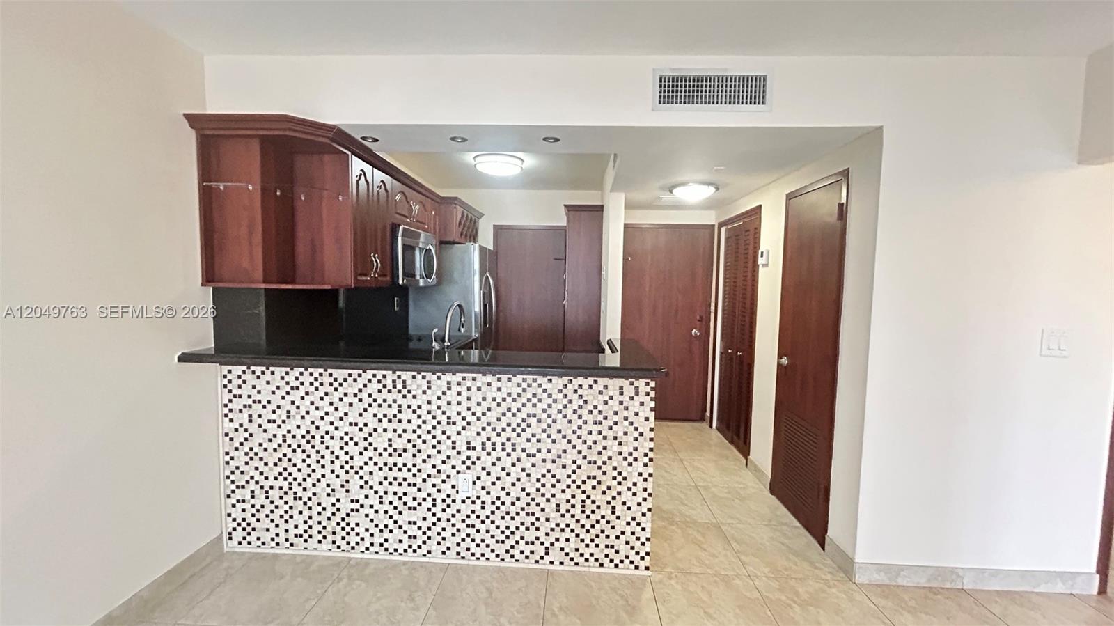 A kitchen features dark wood cabinets, a black countertop, and a mosaic-tiled breakfast bar — 2899 Collins Ave # 938, Miami Beach FL 33140, MIAMI BEACH, FL