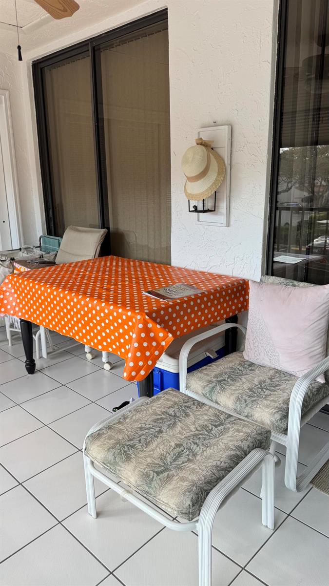 A covered patio features a table with an orange polka-dot cloth and a cushioned chair — 5267 Europa Drive, Boynton Beach FL 33437, BOYNTON BEACH, FL