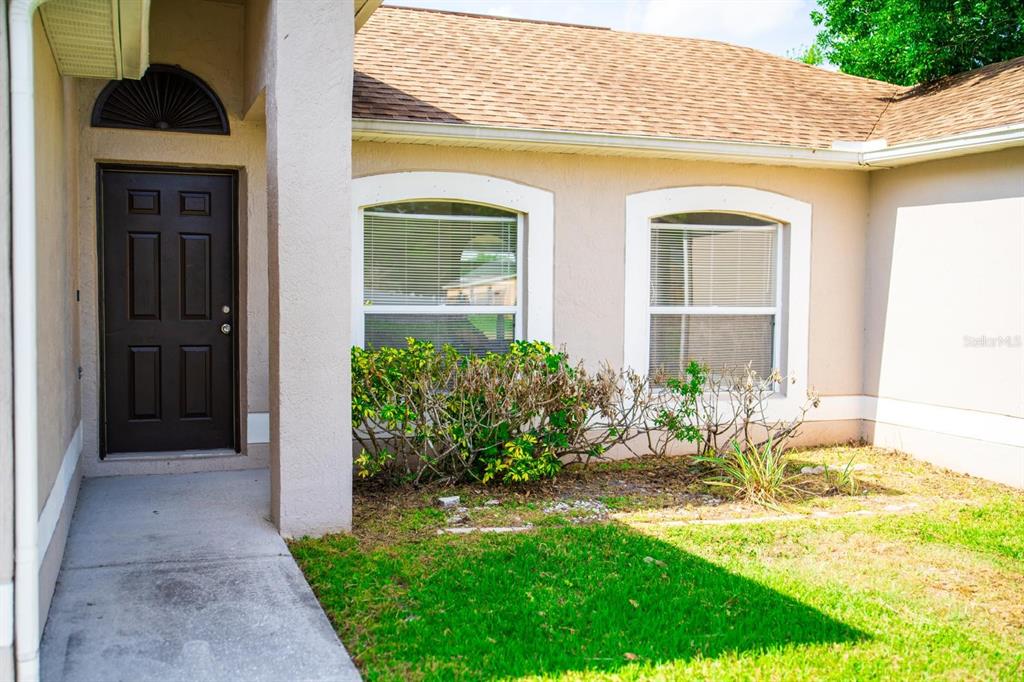 A tan house exterior features a dark front door, two arched windows, and a small garden — 2470 AUGUSTA WAY, KISSIMMEE, FL