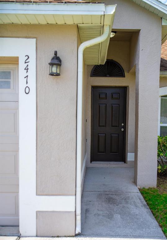 A beige house exterior features a dark brown front door and a white garage door — 2470 AUGUSTA WAY, KISSIMMEE, FL