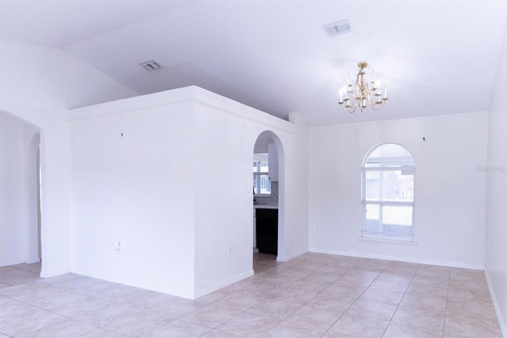 A bright, tiled living area features a white partition wall, arched entryway, and chandelier — 2470 AUGUSTA WAY, KISSIMMEE, FL