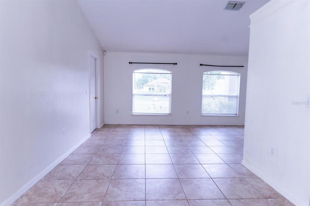 An empty room with light-colored tile flooring, white walls, and two arched windows — 2470 AUGUSTA WAY, KISSIMMEE, FL