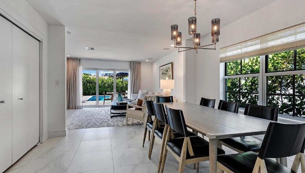 A dining area with a modern chandelier leads to a living room overlooking a pool — 406 35th Street, West Palm Beach FL 33407, WEST PALM BEACH, FL