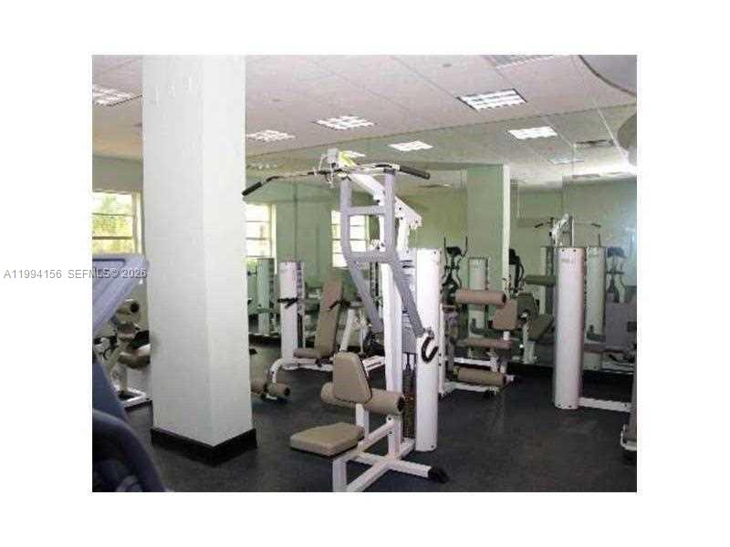 A gym room features several weight machines, a large support pillar, and mirrored walls — 401 69th St # 505, Miami Beach FL 33141, MIAMI BEACH, FL