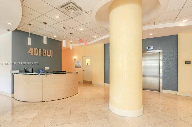 A lobby features a curved reception desk, a large central pillar, and an elevator — 401 69th St # 505, Miami Beach FL 33141, MIAMI BEACH, FL