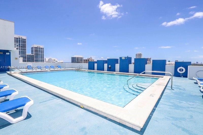 A rooftop swimming pool features blue lounge chairs and a view of city buildings — 401 69th St # 505, Miami Beach FL 33141, MIAMI BEACH, FL
