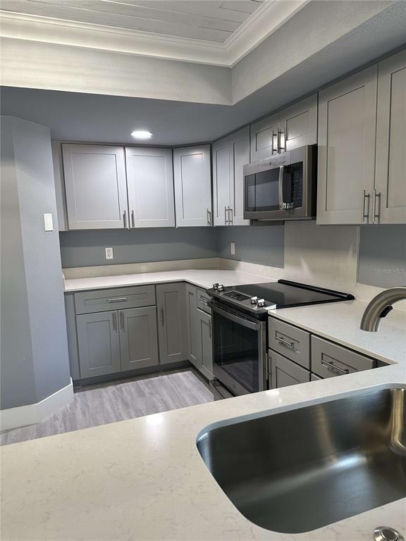 A kitchen features gray shaker cabinets, white countertops, stainless steel appliances, and light wood flooring — 14 MID PINES CIRCLE UNIT 14, PALM COAST, FL