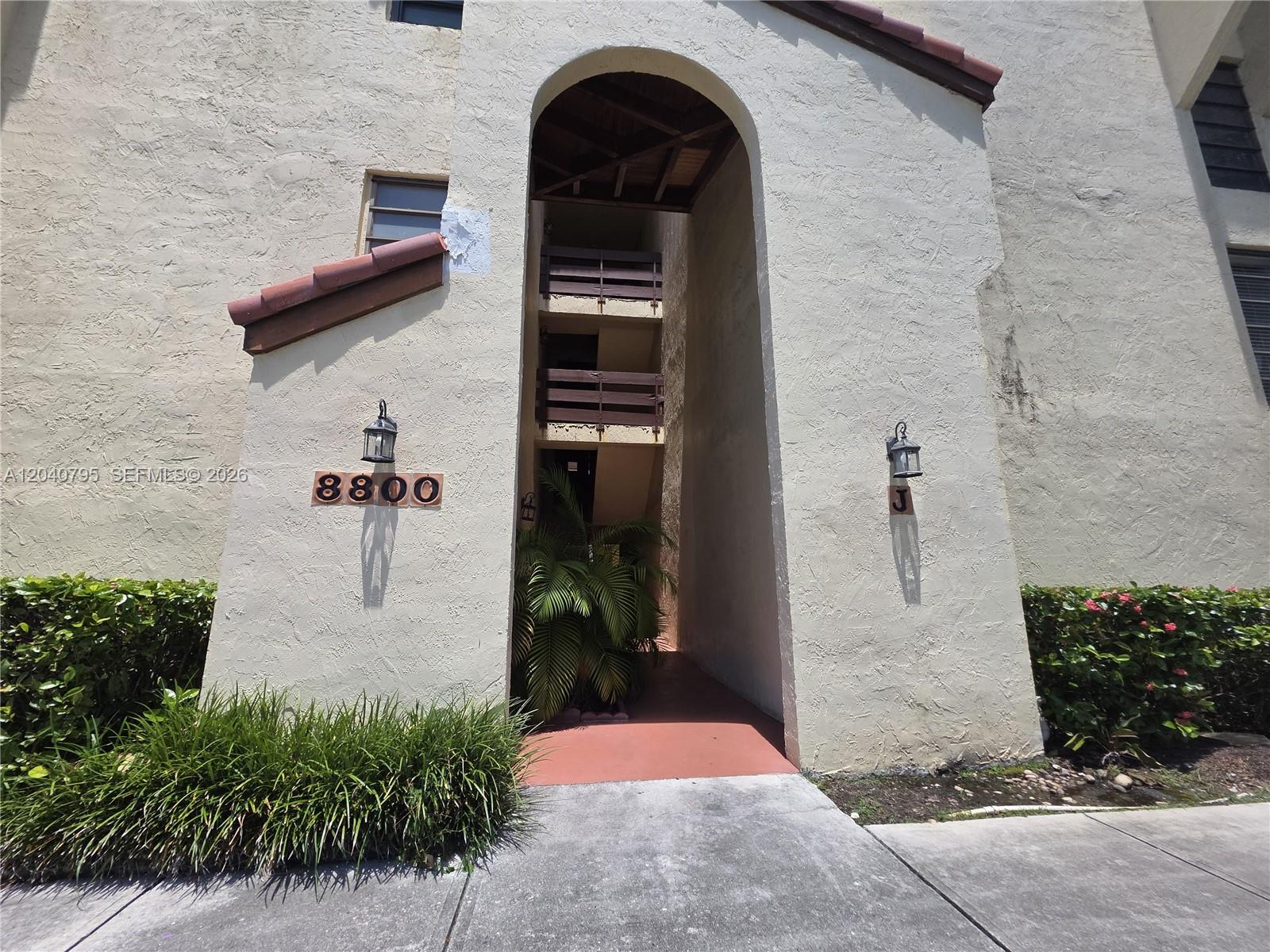 The exterior of a multi-story apartment building features a large arched entryway and stucco walls — 8800 SW 123rd Ct # J105, Miami FL 33186, MIAMI, FL