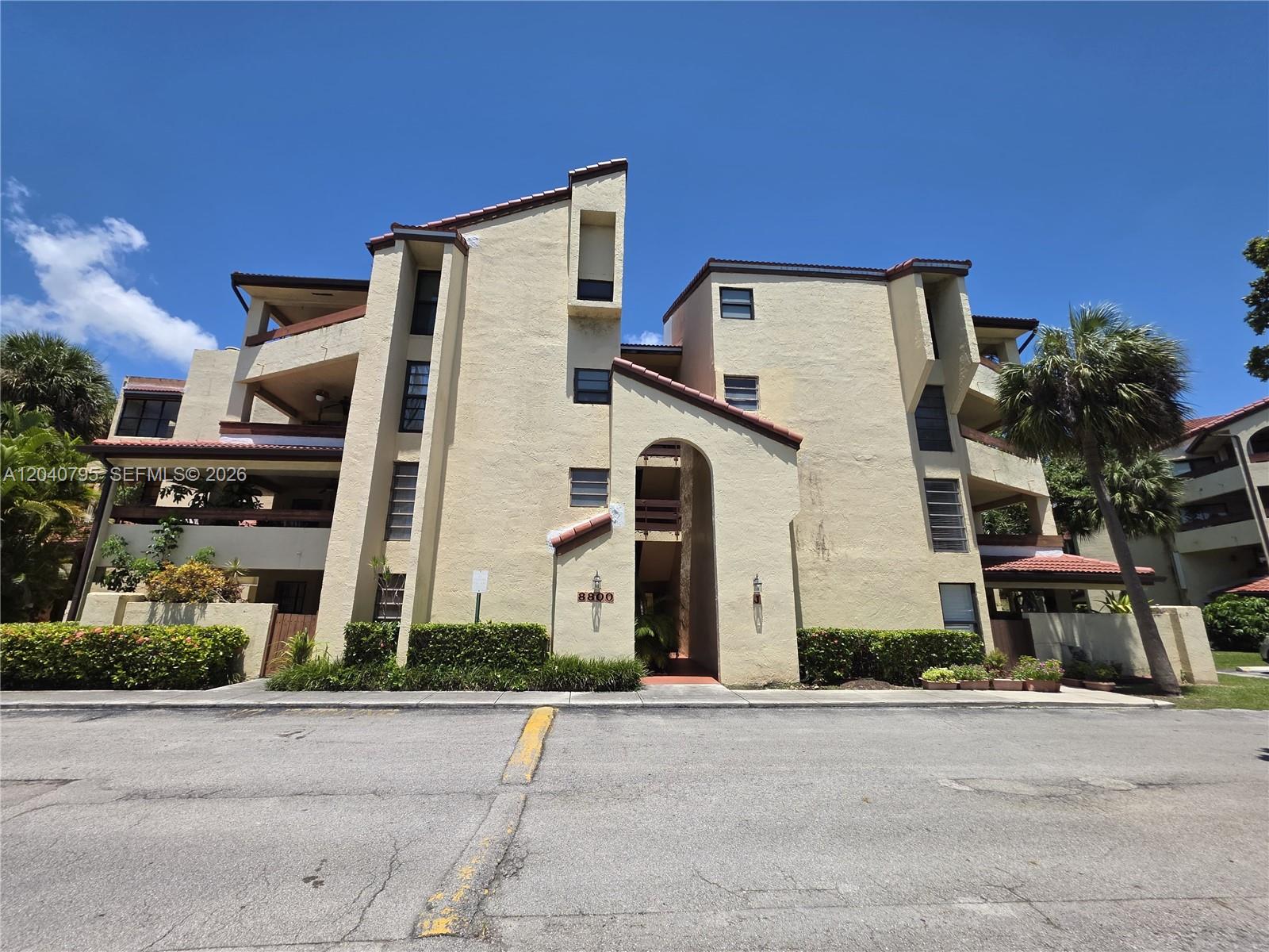 A multi-story beige stucco apartment building with a central arched entryway and tiled roof — 8800 SW 123rd Ct # J105, Miami FL 33186, MIAMI, FL