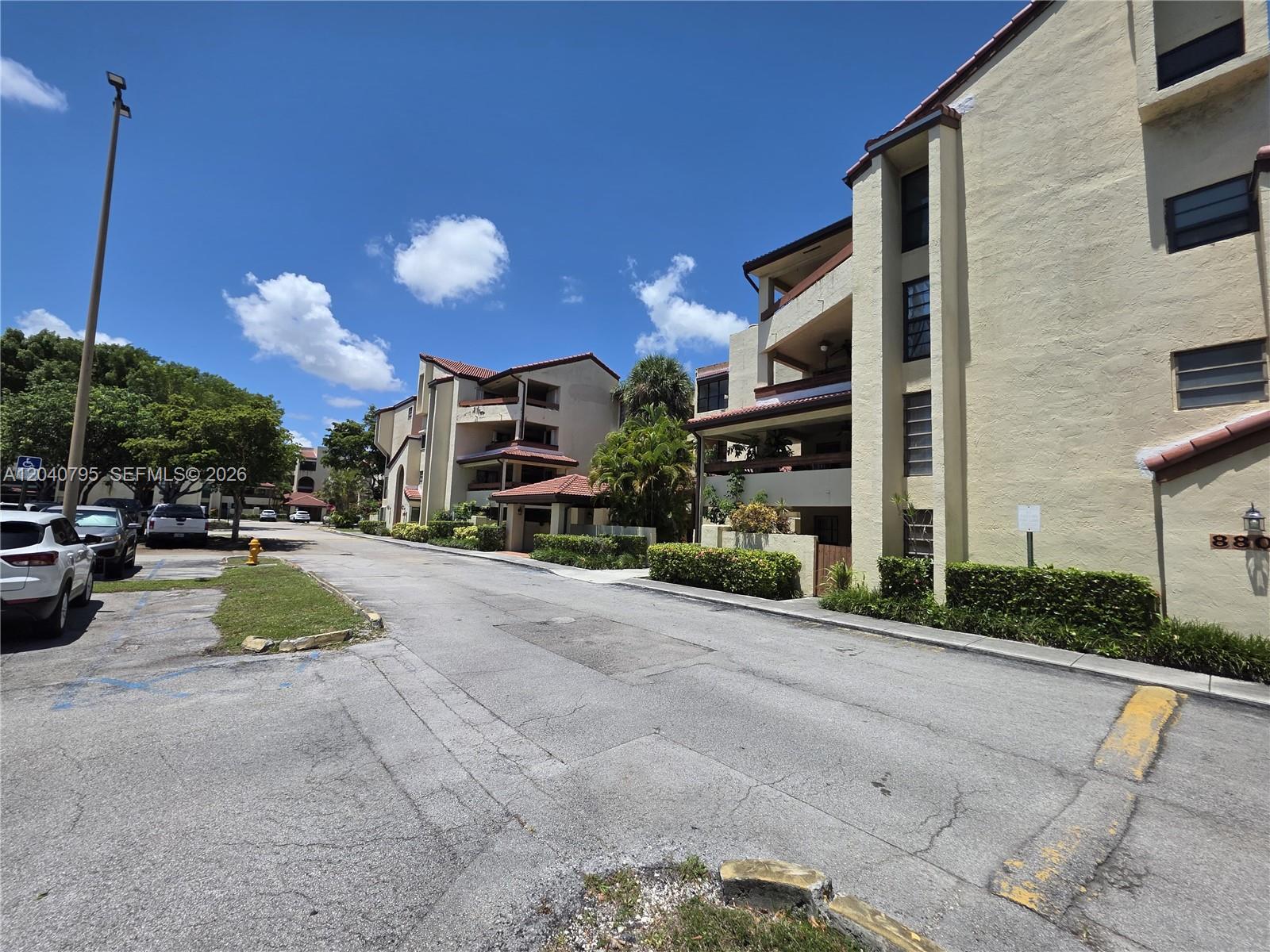 A paved road leads past multi-story apartment buildings with stucco walls and tiled roofs — 8800 SW 123rd Ct # J105, Miami FL 33186, MIAMI, FL