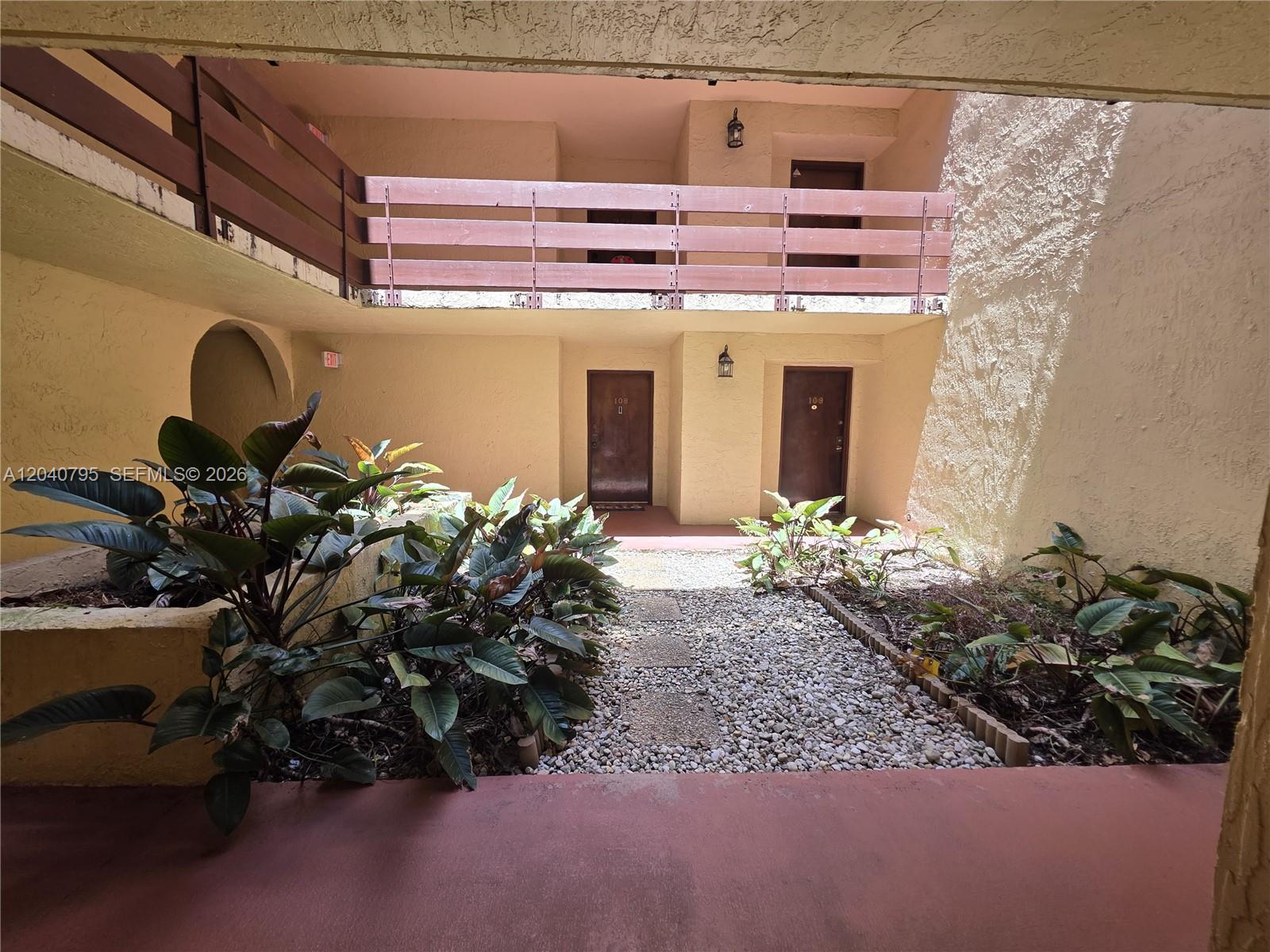 An outdoor courtyard features a gravel path, tropical plants, and two levels of apartment entrances — 8800 SW 123rd Ct # J105, Miami FL 33186, MIAMI, FL