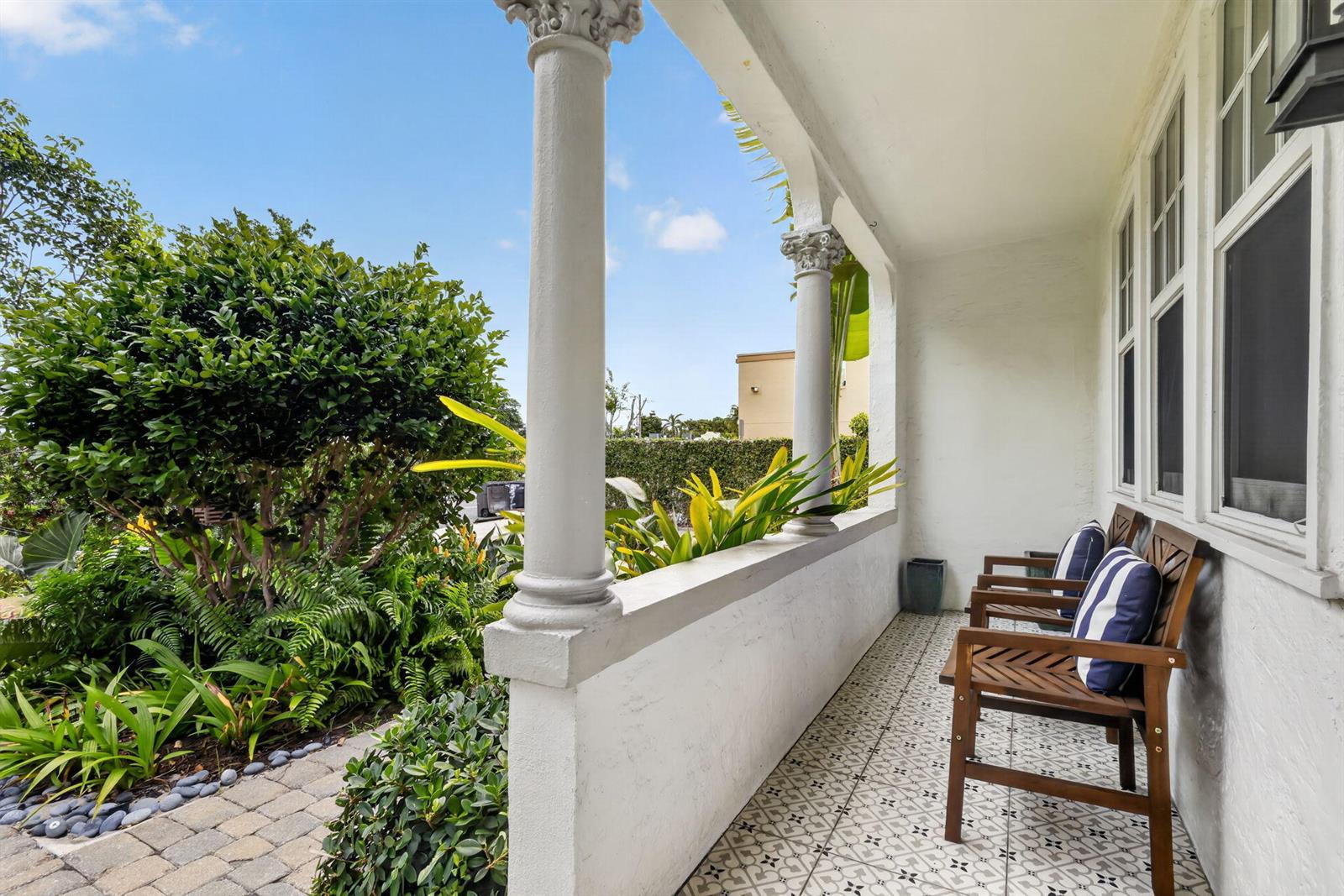 A white covered porch features decorative columns, patterned tile flooring, and two wooden chairs — 412 El Prado, West Palm Beach FL 33405, WEST PALM BEACH, FL