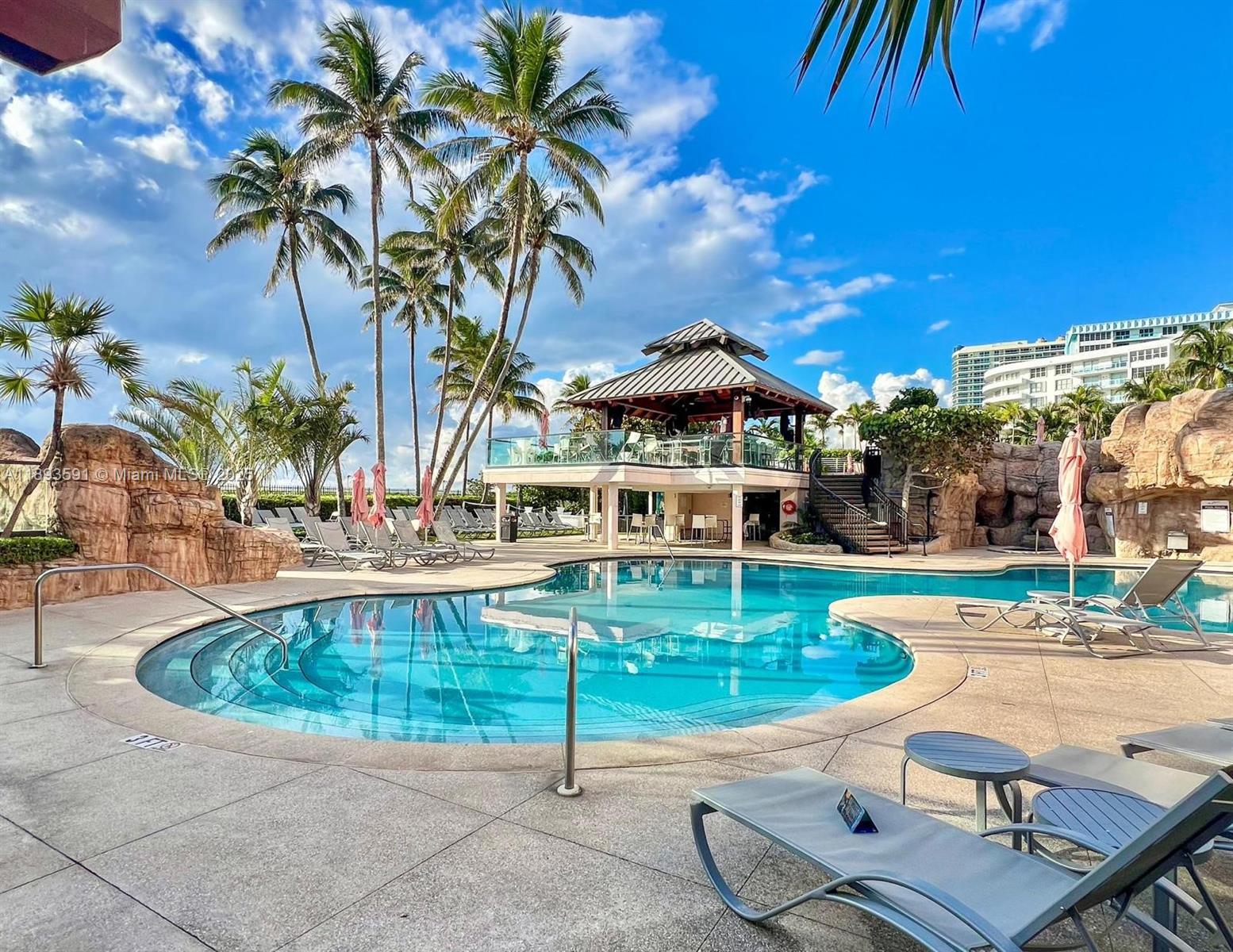 A swimming pool with a gazebo, lounge chairs, and palm trees under a blue sky — 5225 Collins Ave # 517, Miami Beach FL 33140, MIAMI BEACH, FL