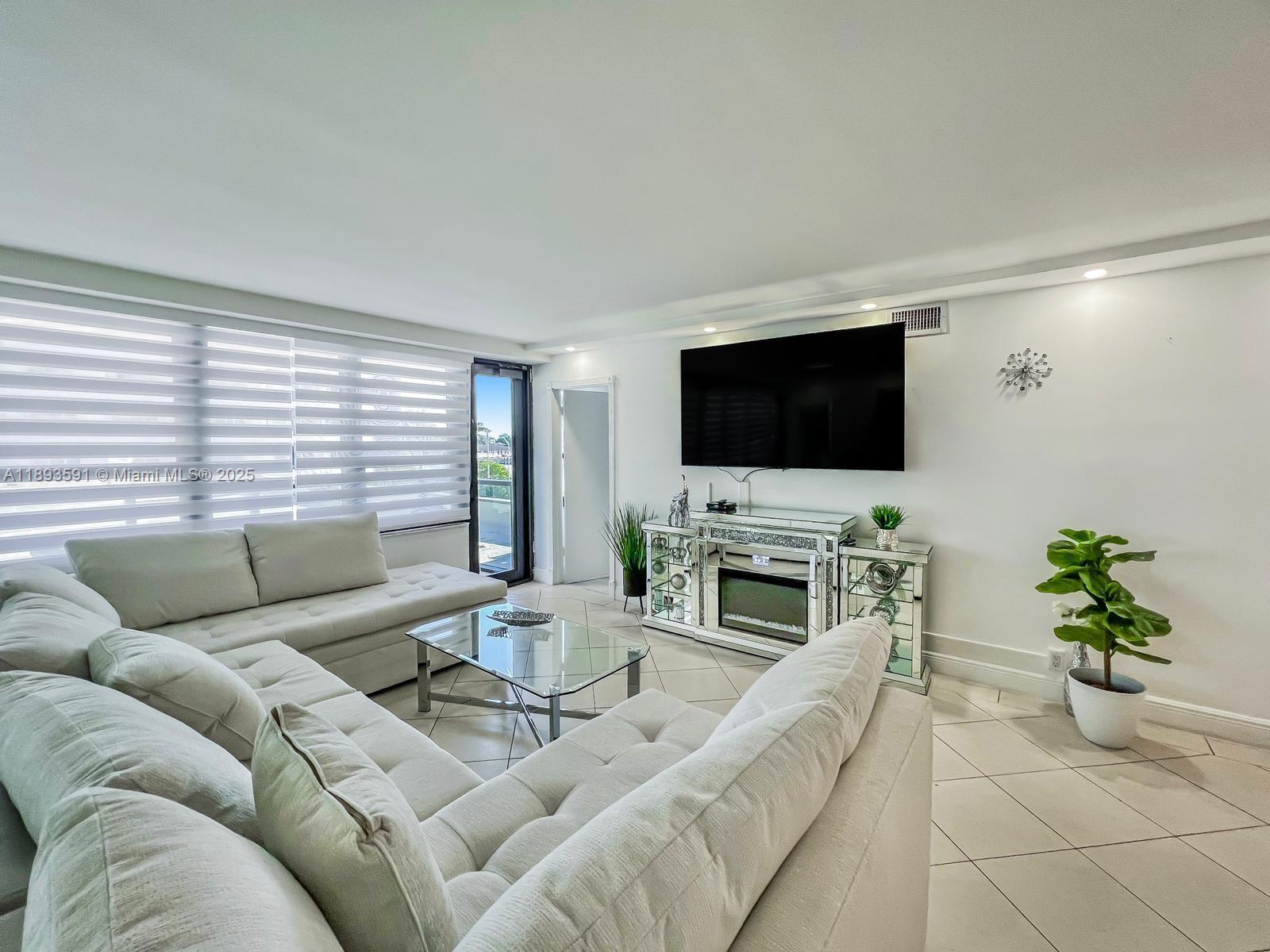 A living room features a large sectional sofa, a glass coffee table, and mirrored media console — 5225 Collins Ave # 517, Miami Beach FL 33140, MIAMI BEACH, FL