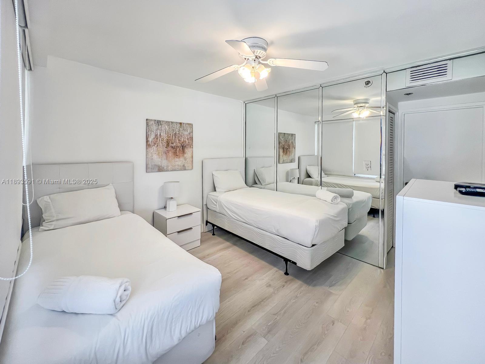 A bedroom features two twin beds, light wood flooring, and a large mirrored closet wall — 5225 Collins Ave # 517, Miami Beach FL 33140, MIAMI BEACH, FL