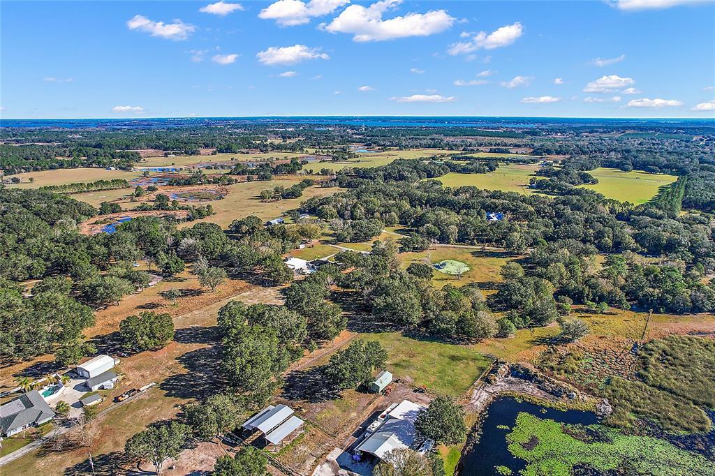 An aerial view shows a rural property with multiple buildings, trees, and a large pond — 0000 SILVERWOOD LANE, HOWEY IN THE HILLS, FL