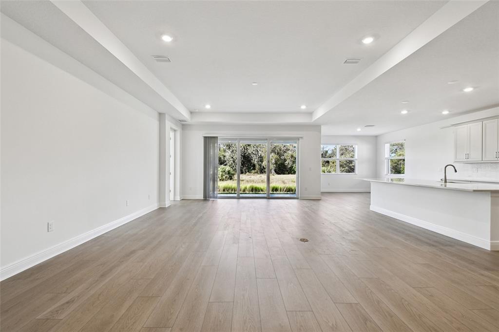 An open-concept living area features light wood-look flooring, white walls, and a modern kitchen — 3673 3673 142ND TER E, PARRISH, FL