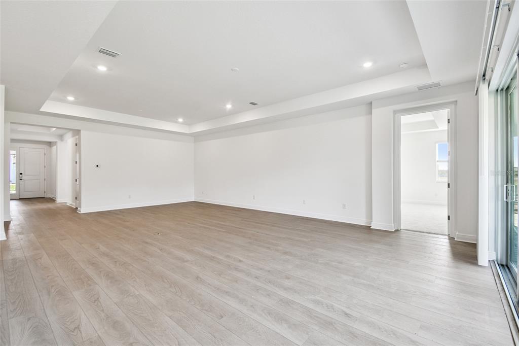 An empty living room features light wood-look flooring, white walls, and a tray ceiling — 3673 3673 142ND TER E, PARRISH, FL