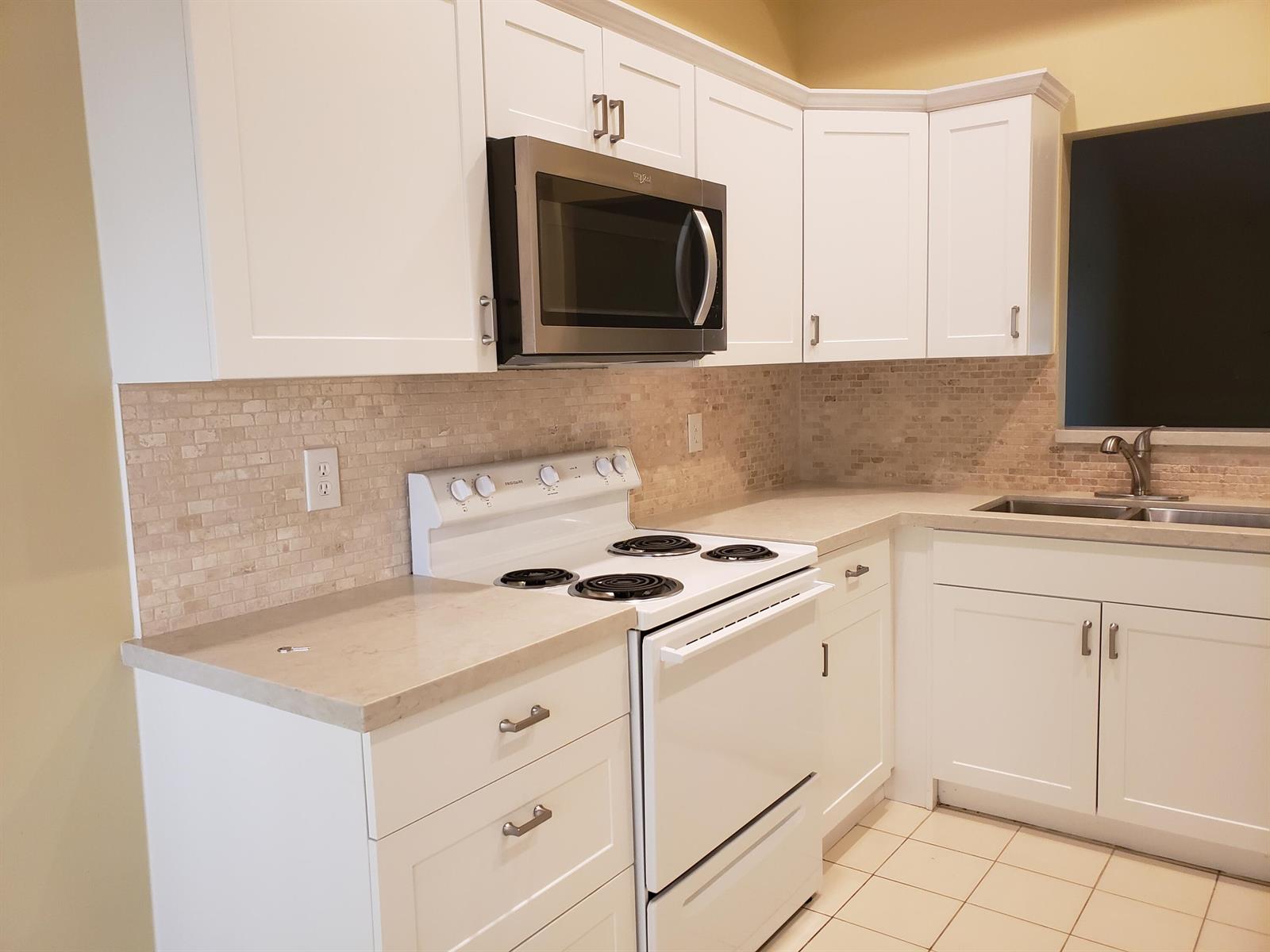 A kitchen features white cabinets, a stainless steel microwave, a white stove, and tile backsplash — 10875 Lake Front Place # 10875, Boca Raton FL 33498, BOCA RATON, FL