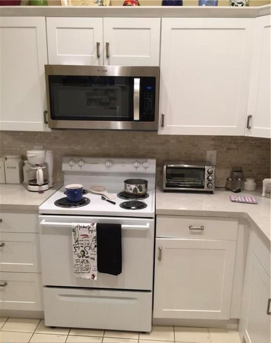 A kitchen features white cabinets, a stainless steel microwave, and a white freestanding range — 10875 Lake Front Place # 10875, Boca Raton FL 33498, BOCA RATON, FL