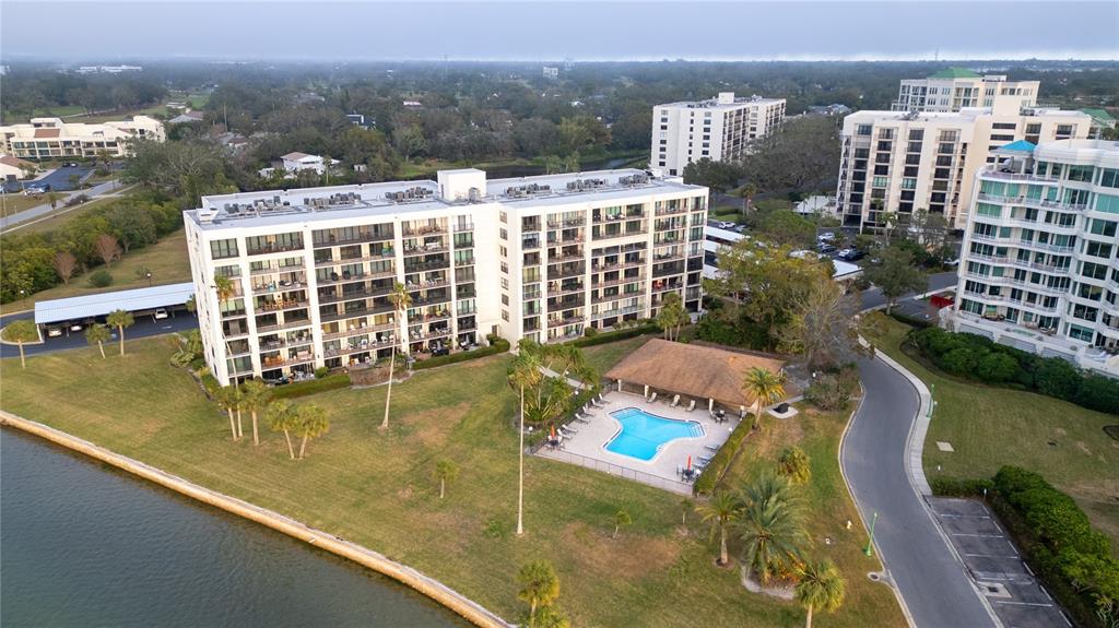An aerial view shows a multi-story apartment building with a pool and a thatched-roof cabana — 100 OAKMONT LANE UNIT 605, BELLEAIR, FL