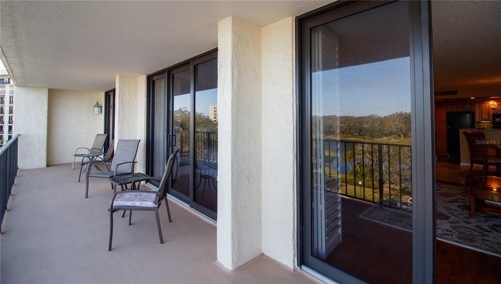 A balcony with outdoor chairs overlooks a lake and trees through sliding glass doors — 100 OAKMONT LANE UNIT 605, BELLEAIR, FL
