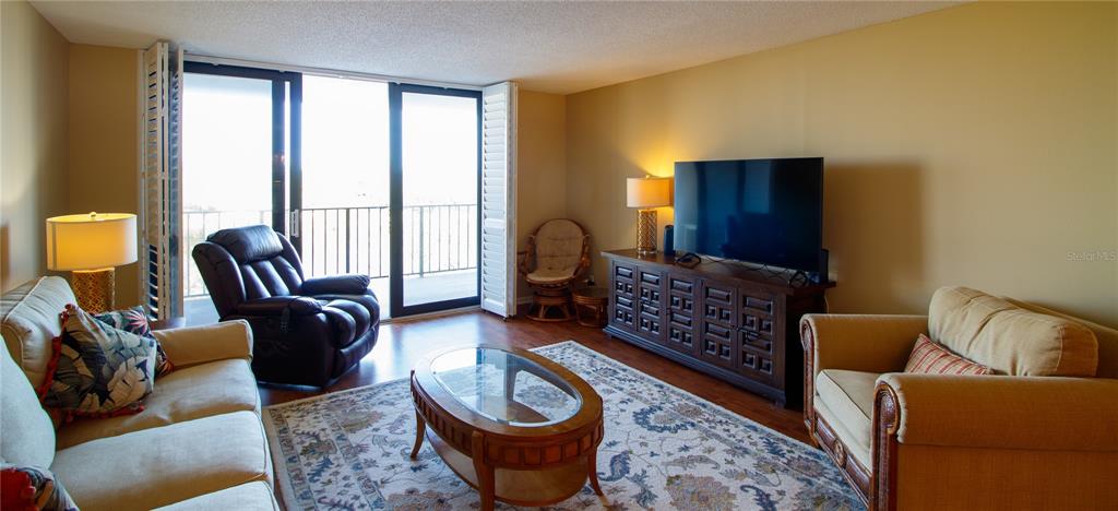 A living room features a sofa, recliner, armchair, television on a console, and a balcony — 100 OAKMONT LANE UNIT 605, BELLEAIR, FL