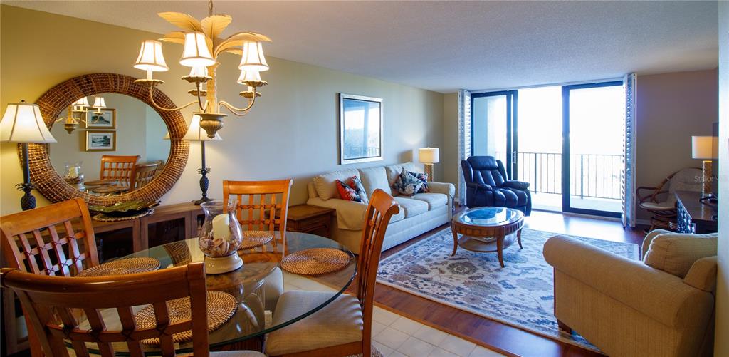 An open-concept living and dining area features a glass table, sofa, and balcony access — 100 OAKMONT LANE UNIT 605, BELLEAIR, FL
