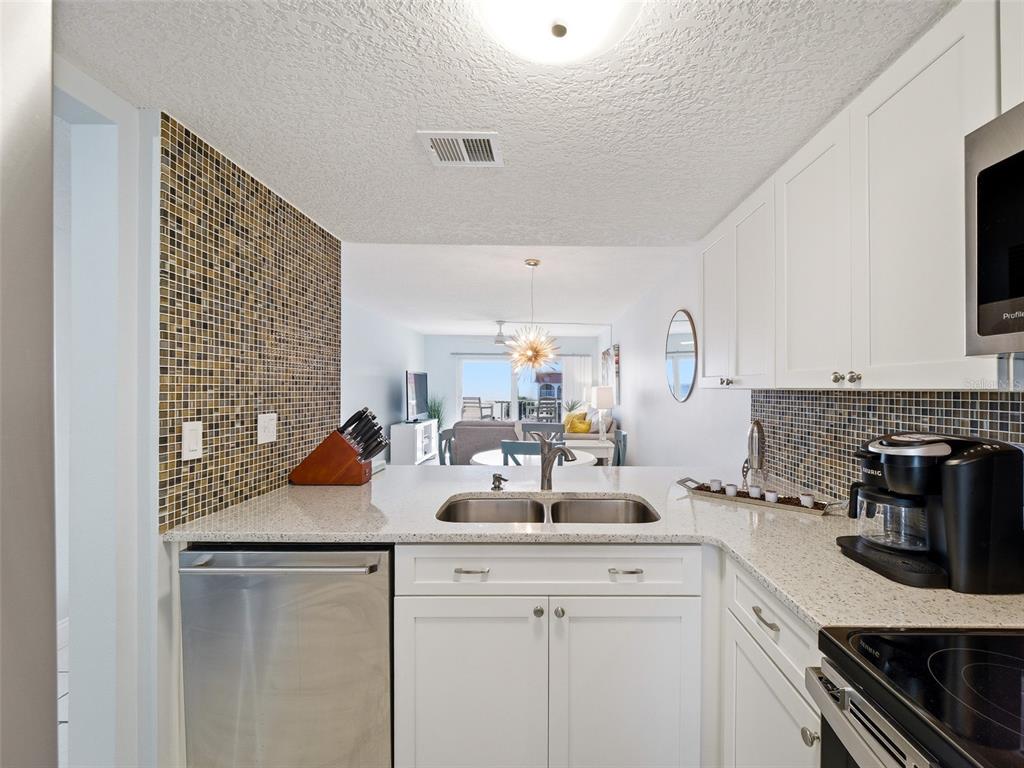 A kitchen with white cabinets, granite countertops, and a mosaic tile backsplash overlooks a living area — 3801 S ATLANTIC AVENUE UNIT 316, NEW SMYRNA BEACH, FL