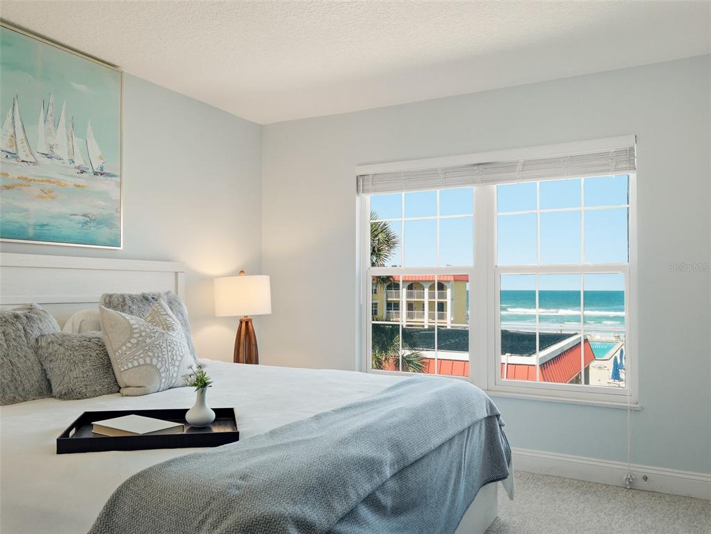A bedroom with a white bed, a coastal painting, and a window overlooking the ocean — 3801 S ATLANTIC AVENUE UNIT 316, NEW SMYRNA BEACH, FL