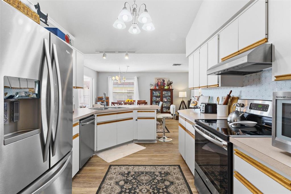 A kitchen with white cabinets, stainless steel appliances, and a patterned rug on wood flooring — 17209 SE 115TH TERRACE ROAD, SUMMERFIELD, FL
