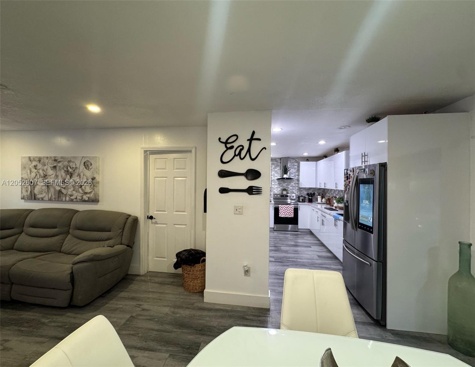A living room with a gray sofa leads into a kitchen featuring white cabinets — 10660 SW 164th St, Miami FL 33157, MIAMI, FL