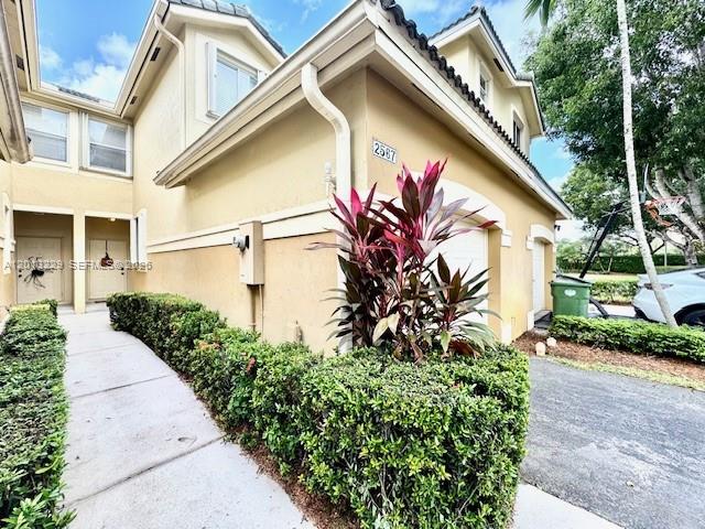 A tan two-story townhouse exterior features a walkway, manicured hedges, and a red-leafed plant — 2567 Cordoba Bnd, Weston FL 33327, WESTON, FL