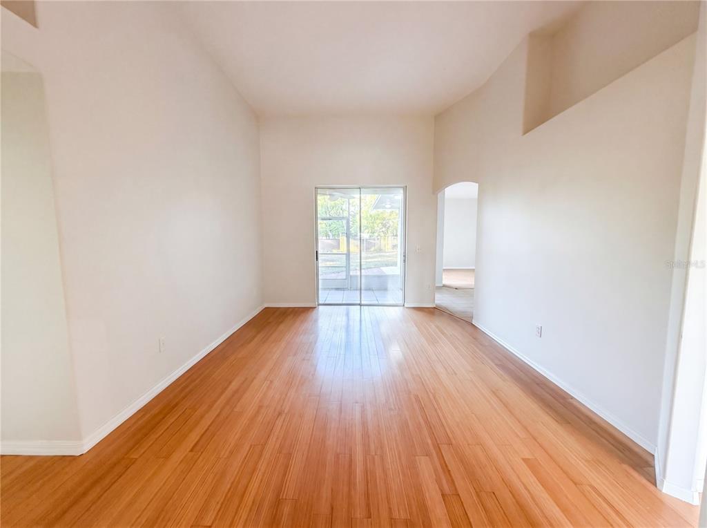An empty room with light wood flooring, high ceilings, and sliding glass doors to a patio — 203 TAYLOR BAY LANE, BRANDON, FL
