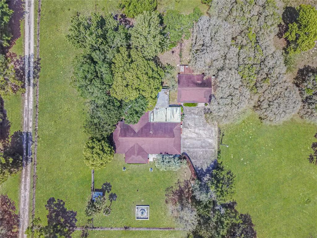 An aerial view shows a house with a brown roof, a concrete driveway, and surrounding trees — 8225 E HIGHWAY 25, BELLEVIEW, FL