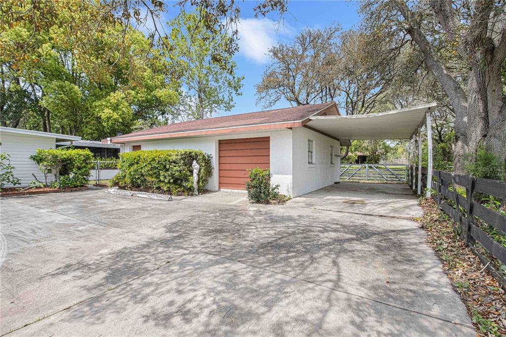 A detached garage with a carport and a concrete driveway sits on a grassy lot — 8225 E HIGHWAY 25, BELLEVIEW, FL