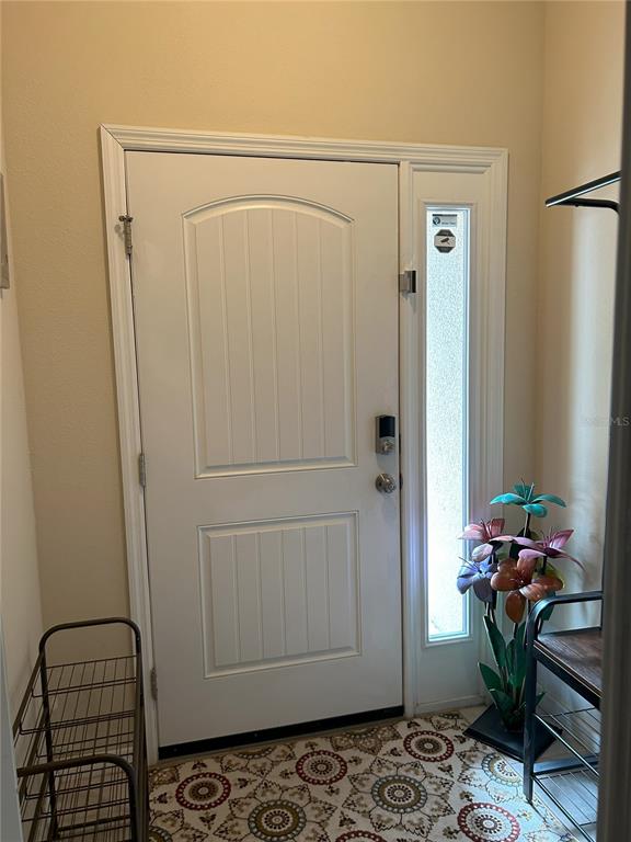 An entryway features a white front door with a sidelight, patterned rug, and metal furniture — 844 CALLISTA CAY LOOP, TARPON SPRINGS, FL