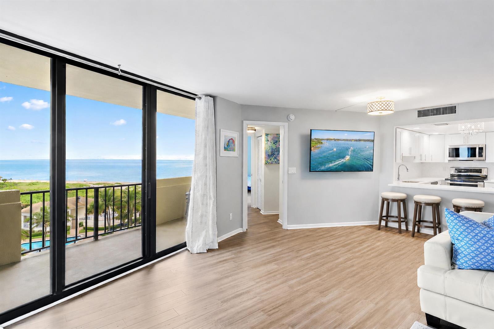 A living room with light wood floors, a wall-mounted television, and a balcony overlooking the ocean — 2800 N Ocean Drive # 7c, Singer Island FL 33404, SINGER ISLAND, FL