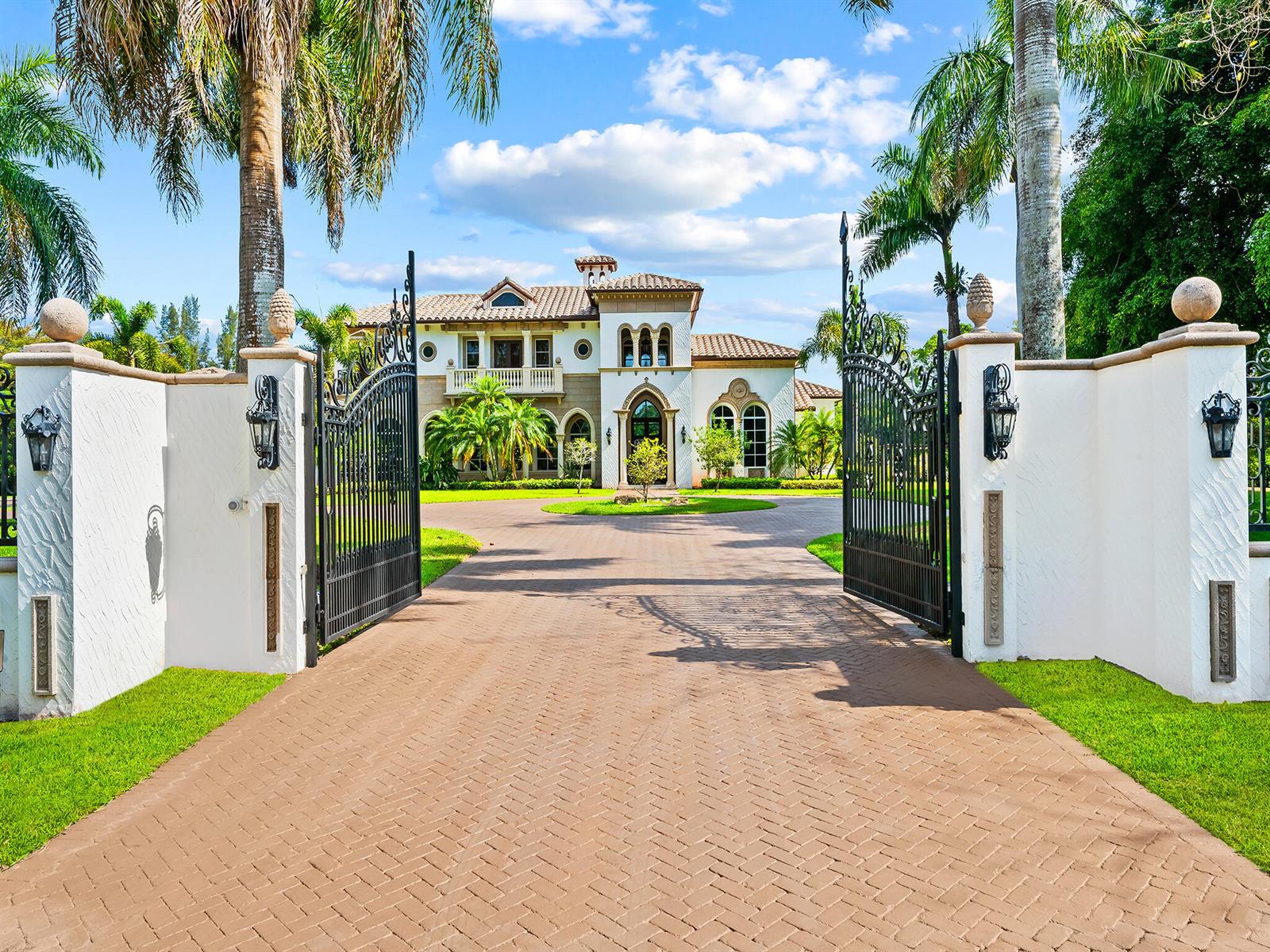A paved driveway leads through an open iron gate toward a large Mediterranean-style house — 8800 NW 68th Court, Parkland FL 33067, PARKLAND, FL