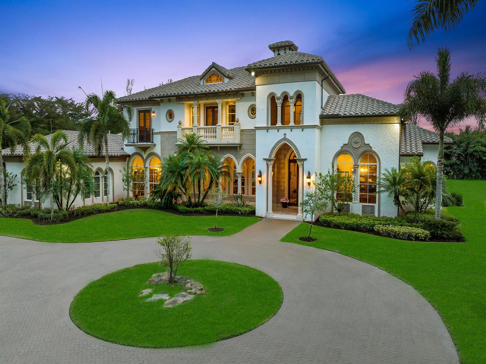 A large two-story Mediterranean-style house with a circular driveway and palm trees at dusk — 8800 NW 68th Court, Parkland FL 33067, PARKLAND, FL