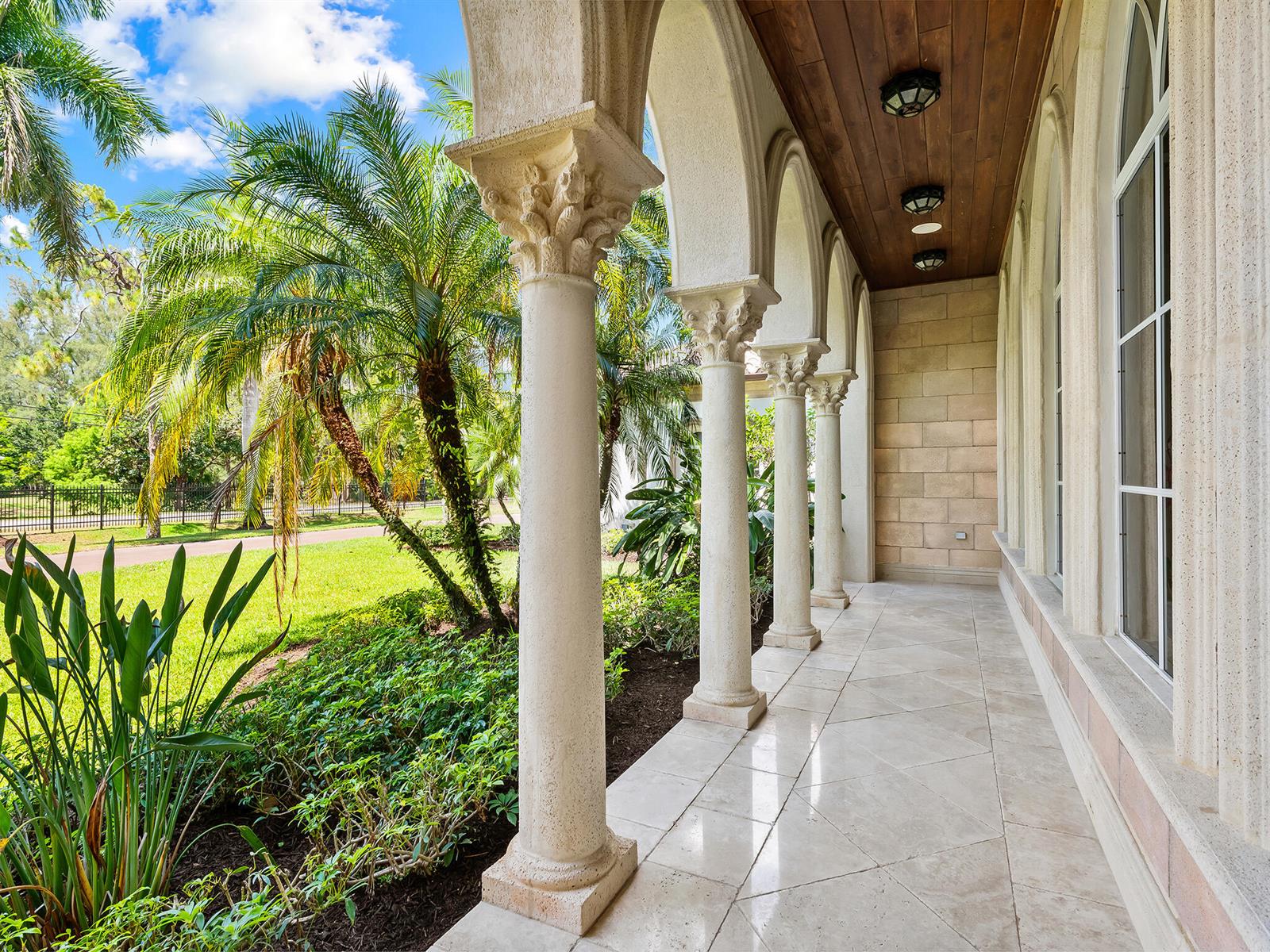 A covered stone patio features arched columns, a wood ceiling, and views of palm trees — 8800 NW 68th Court, Parkland FL 33067, PARKLAND, FL