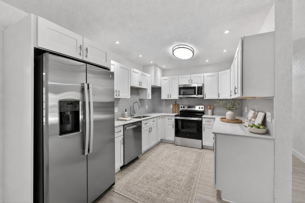 A kitchen featuring white cabinets, stainless steel appliances, gray tile backsplash, and a patterned rug — 1048 SW 1st Terrace, Pompano Beach FL 33060, POMPANO BEACH, FL