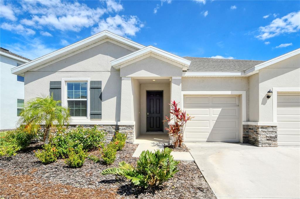 A single-story house with a beige stucco exterior, a stone base, and a front-facing garage — 16921 HARVEST MOON WAY, BRADENTON, FL