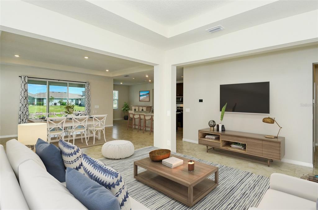 A living room with a television, wooden media console, coffee table, and adjacent dining area — 16921 HARVEST MOON WAY, BRADENTON, FL