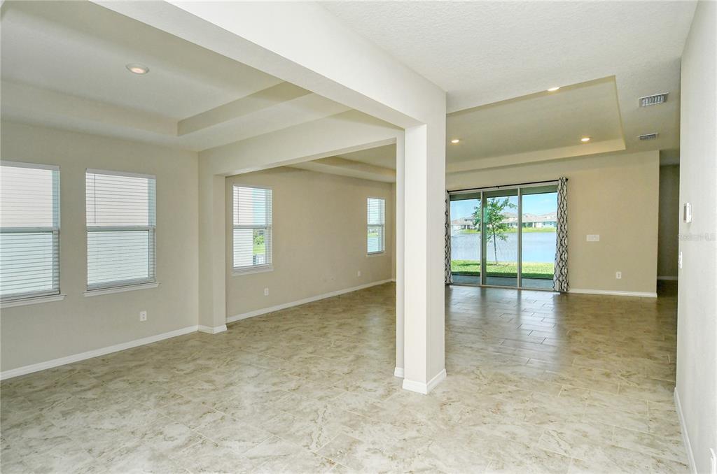An open-concept living area features light-colored tile flooring, tray ceilings, and sliding glass doors — 16921 HARVEST MOON WAY, BRADENTON, FL