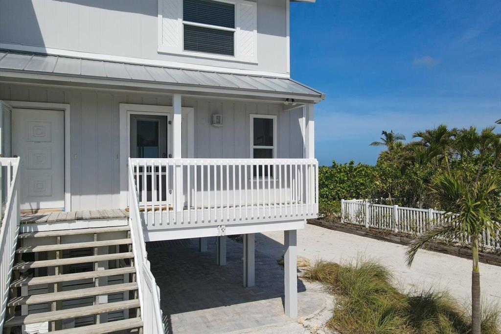 An elevated house with a white porch, stairs, and a sandy yard near the ocean — 420 GULF BOULEVARD UNIT 13, BOCA GRANDE, FL